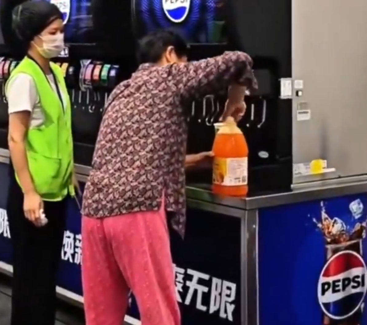 在武漢的一間山姆超市,一位中年大媽在飲食區手持大膠樽,在店內免費添飲續杯飲料吧裝滿了一整桶飲料,不顧員工在旁勸阻(影片截圖)