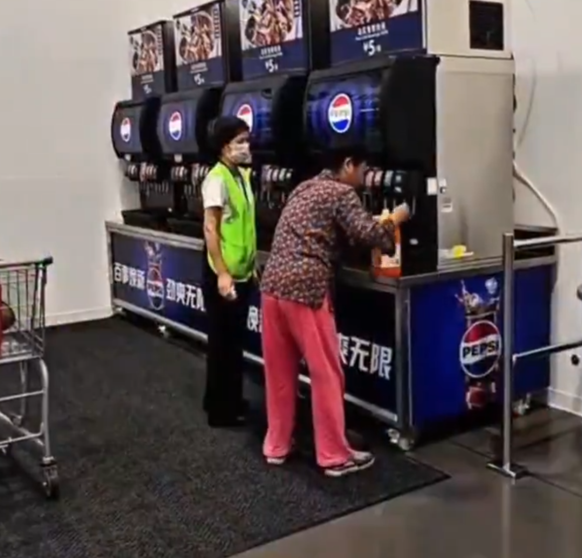 在武漢的一間山姆超市,一位中年大媽在飲食區手持大膠樽,在店內免費添飲續杯飲料吧裝滿了一整桶飲料,不顧員工在旁勸阻(影片截圖)