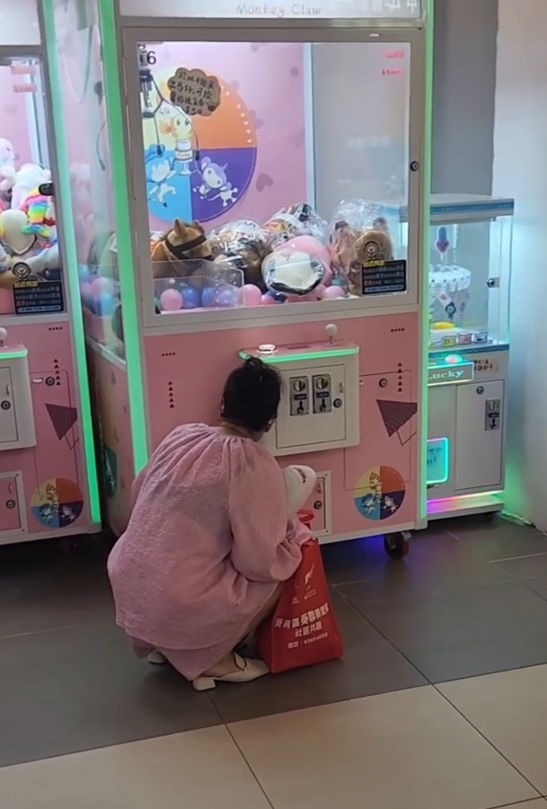 一名疑似母親蹲在夾公仔機前面,一名女童竟然鑽入機內出貨口位置(Threads影片截圖)