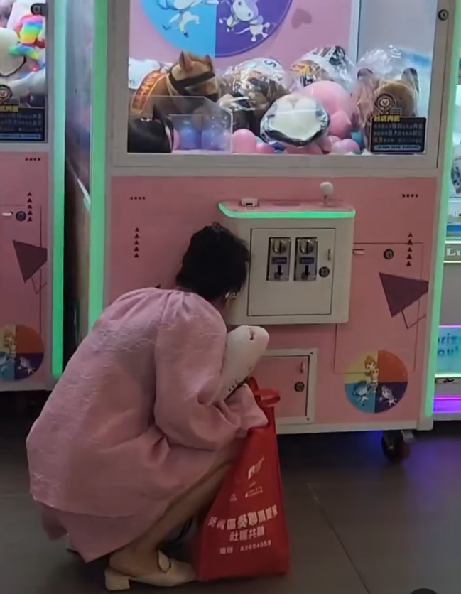 一名疑似母親蹲在夾公仔機前面,一名女童竟然鑽入機內出貨口位置(Threads影片截圖)