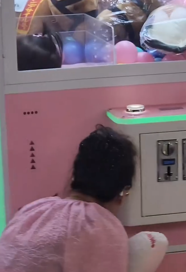 一名疑似母親蹲在夾公仔機前面,一名女童竟然鑽入機內出貨口位置(Threads影片截圖)
