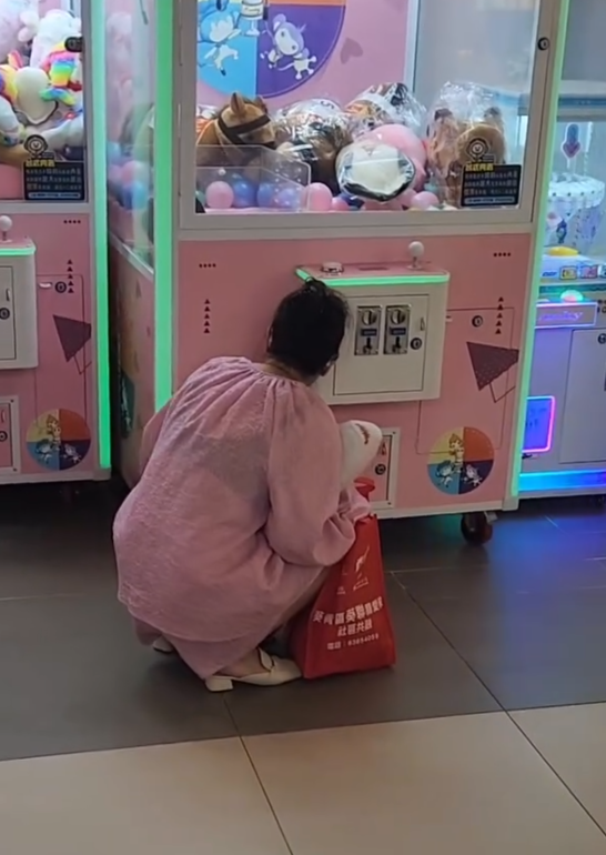 一名疑似母親蹲在夾公仔機前面,一名女童竟然鑽入機內出貨口位置(Threads影片截圖)
