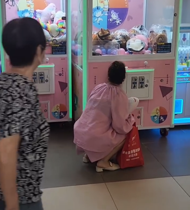 一名疑似母親蹲在夾公仔機前面,一名女童竟然鑽入機內出貨口位置(Threads影片截圖)