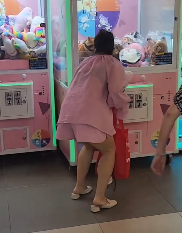一名疑似母親蹲在夾公仔機前面,一名女童竟然鑽入機內出貨口位置(Threads影片截圖)