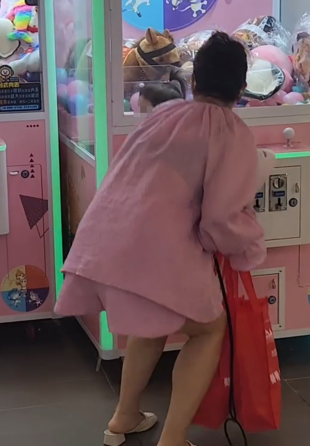 一名疑似母親蹲在夾公仔機前面,一名女童竟然鑽入機內出貨口位置(Threads影片截圖)