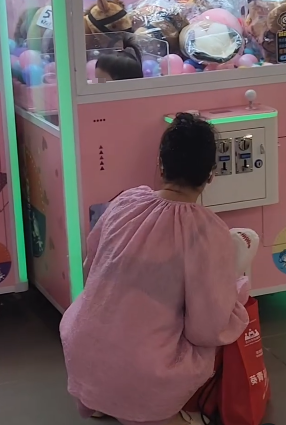 一名疑似母親蹲在夾公仔機前面,一名女童竟然鑽入機內出貨口位置(Threads影片截圖)