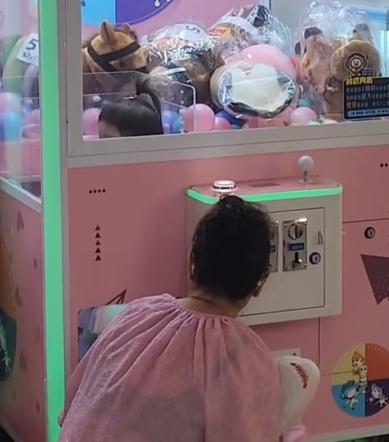 一名疑似母親蹲在夾公仔機前面,一名女童竟然鑽入機內出貨口位置(Threads影片截圖)