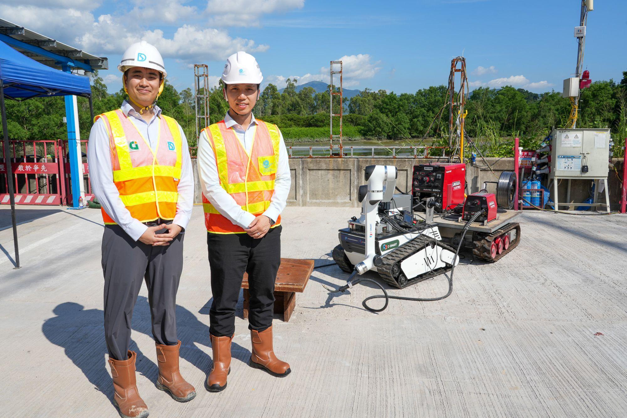 發展局助理秘書長(計劃管理)羅梓馨(右)和渠務署工程師李澤祖(左)介紹「元朗防洪壩及明渠改善計劃」工程中應用的燒焊機械人及遙控天秤系統。