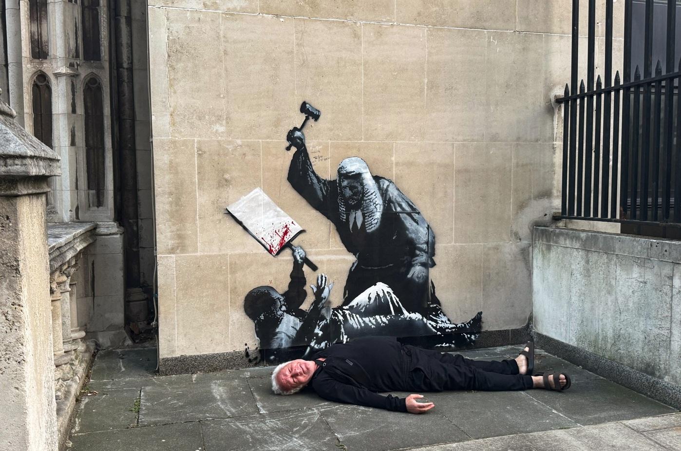 有民眾在Banksy作品前瞓地模仿示威者。(路透社)