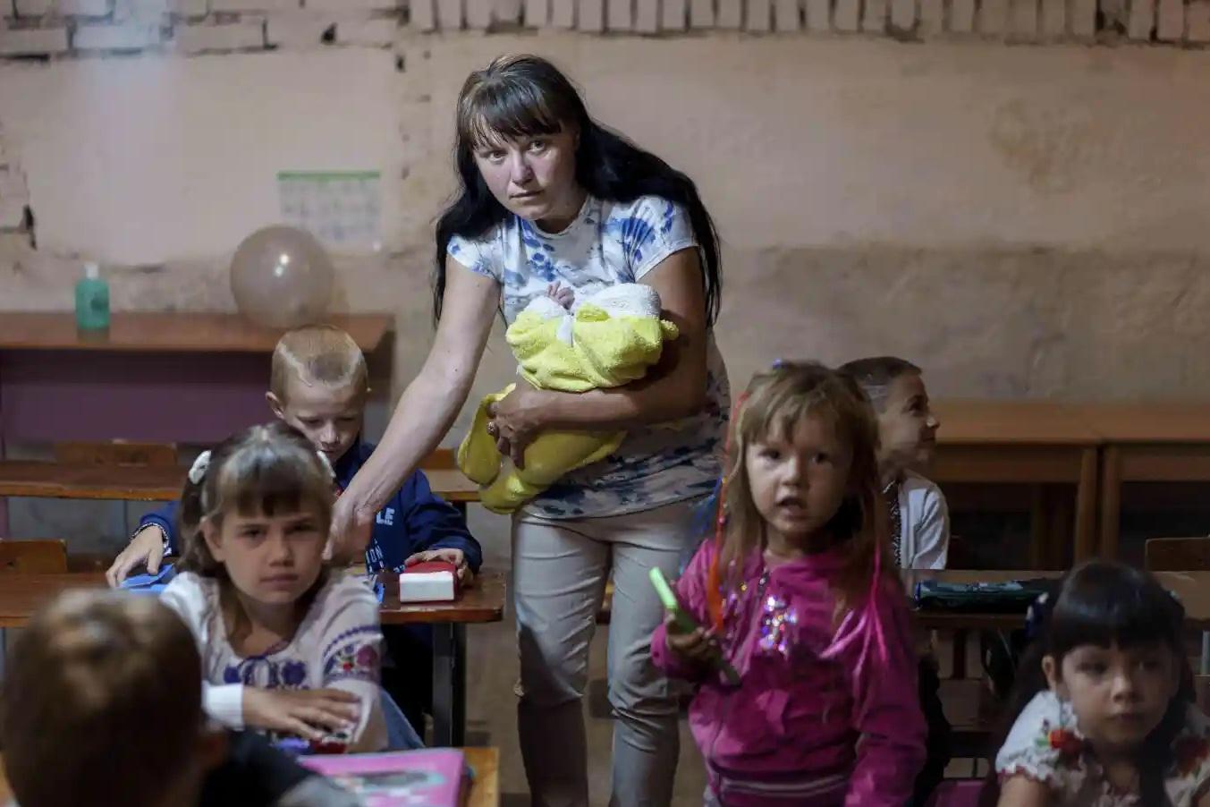 今年9月1日開學日,烏克蘭東北部蘇梅州一些兒童躲在政府大樓的地牢上課,一位母親抱著幼兒照顧學習中的兒子。(資料圖片)