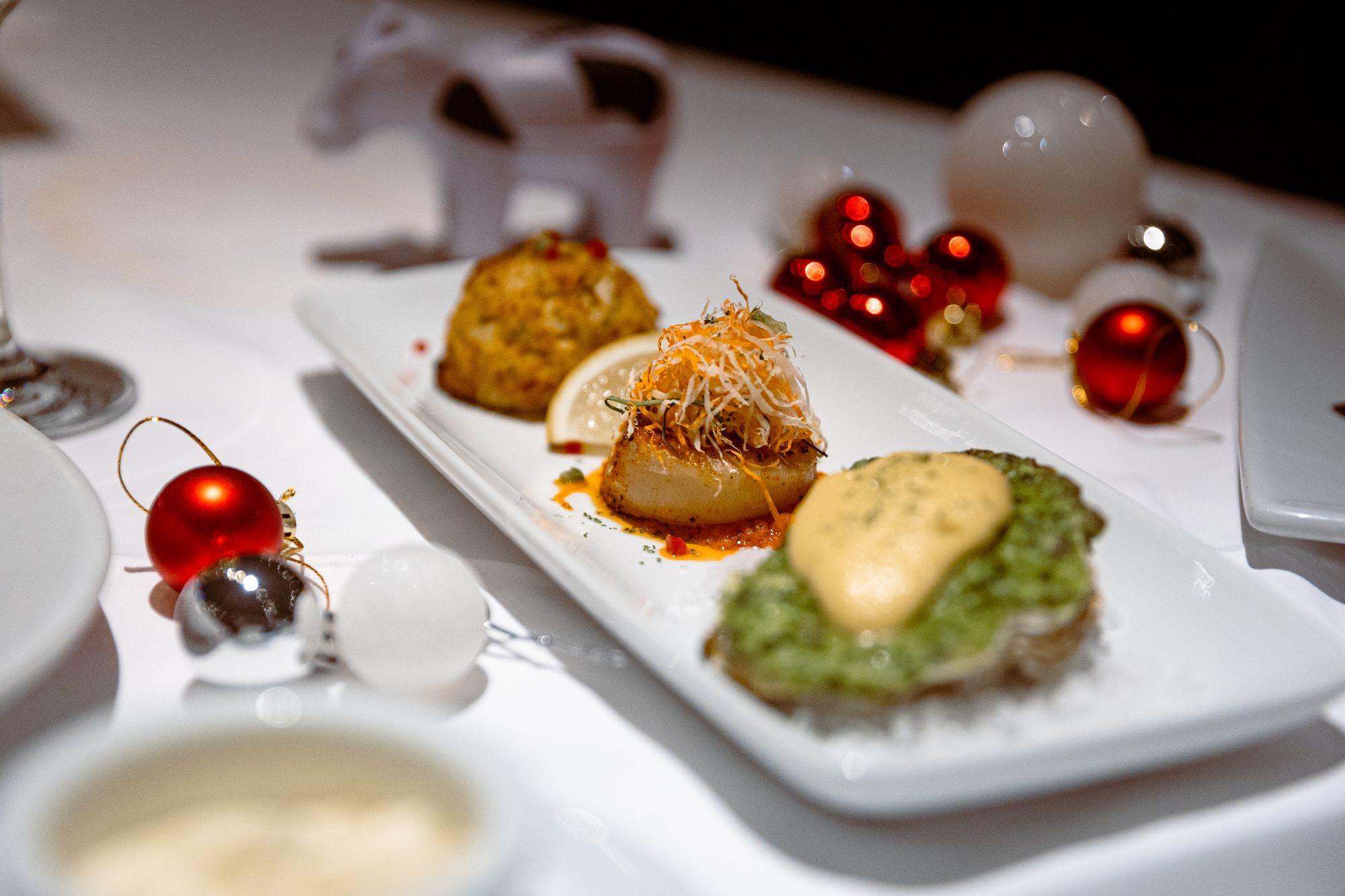 前菜「海鮮三重奏」包括新奧爾良蟹肉糕、香煎乾貝和洛克菲焗烤鮮蠔。