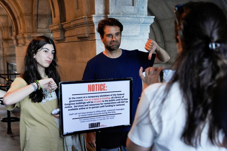 民眾在國會圖書館關閉告示前倒豎拇指拍照,表達不滿。(美聯社)