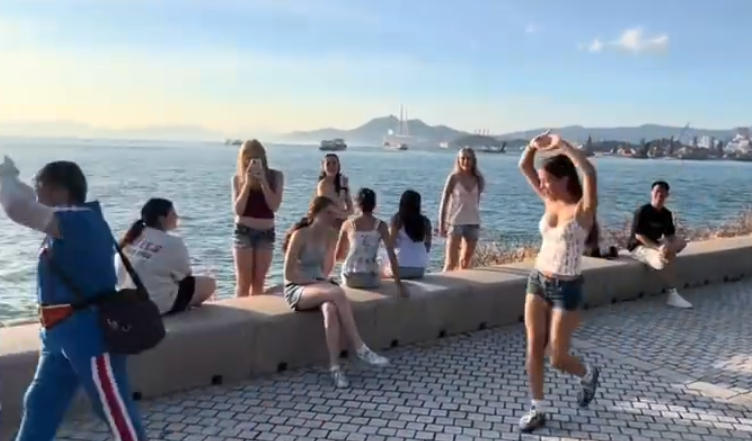 內地屢引發爭議的「暴走團」殺入香港,現身西九文化區徒步和做伸展運動,沿途大聲播放音樂影片,惹來旁邊市民及遊客側目,不過亦有外籍女子好奇之下「加入」隊尾,模仿有關動作。(影片截圖)