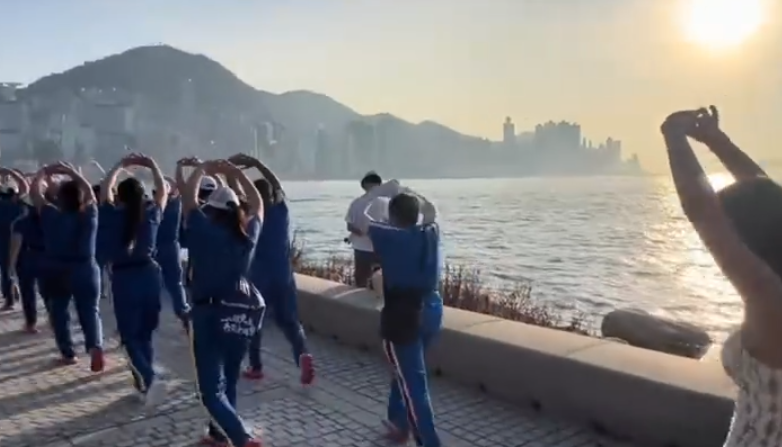 內地屢引發爭議的「暴走團」殺入香港,現身西九文化區徒步和做伸展運動,沿途大聲播放音樂影片,惹來旁邊市民及遊客側目,不過亦有外籍女子好奇之下「加入」隊尾,模仿有關動作。(影片截圖)