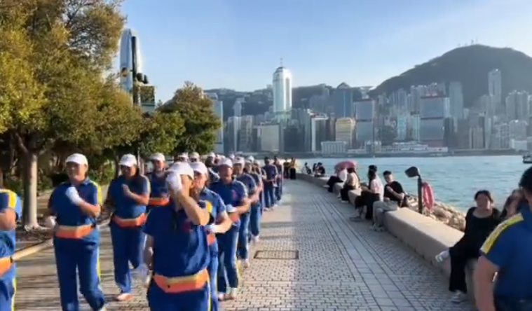 內地屢引發爭議的「暴走團」殺入香港,現身西九文化區徒步和做伸展運動,沿途大聲播放音樂影片,惹來旁邊市民及遊客側目。(影片截圖)