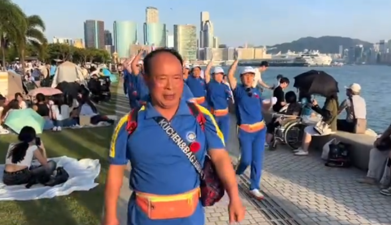 內地屢引發爭議的「暴走團」殺入香港,現身西九文化區徒步和做伸展運動,沿途大聲播放音樂影片,惹來旁邊市民及遊客側目。(影片截圖)