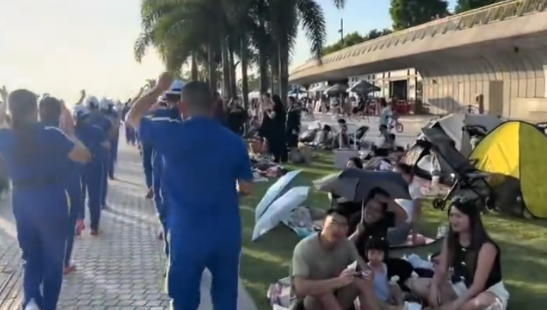 內地屢引發爭議的「暴走團」殺入香港,現身西九文化區徒步和做伸展運動,沿途大聲播放音樂影片,惹來旁邊市民及遊客側目。(影片截圖)