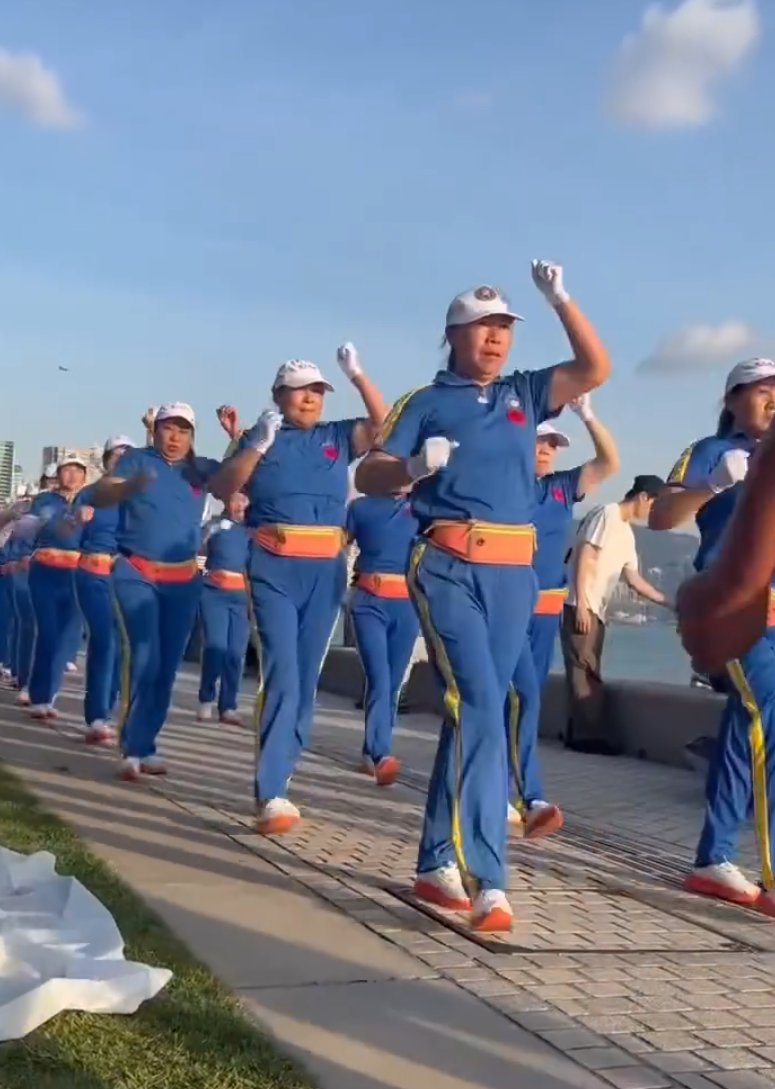 內地屢引發爭議的「暴走團」殺入香港,現身西九文化區徒步和做伸展運動,沿途大聲播放音樂影片,惹來旁邊市民及遊客側目。(影片截圖)