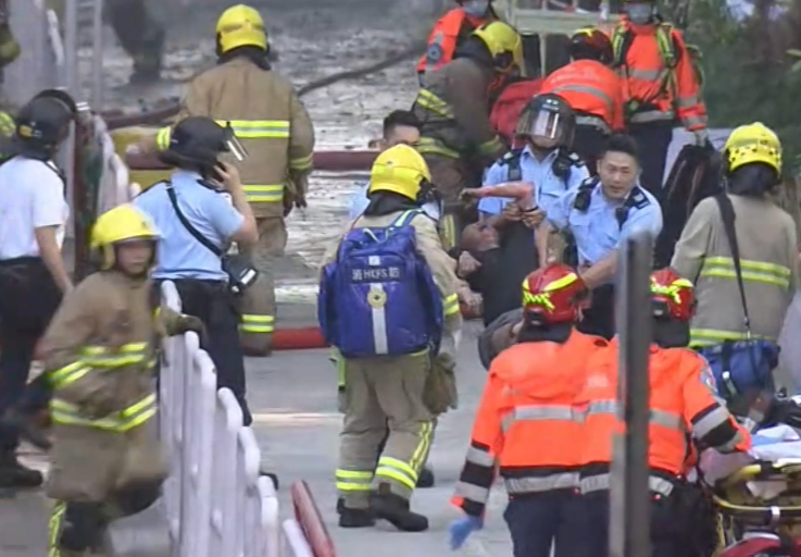 大埔宏福苑宏昌閣外牆棚架起火,有男長者昏迷,由警員送上擔架。(電視畫面)