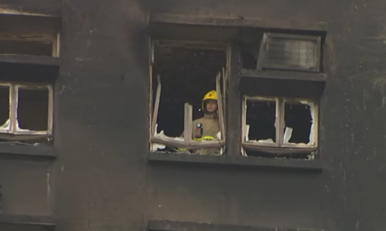 大埔宏福苑五級火,一名消防員登上一個已遭嚴重焚毀、窗框破爛的單位視察,不時望向窗外凝視接近5分鐘,期間若有所思神色凝重咬唇。(有線新聞畫面)