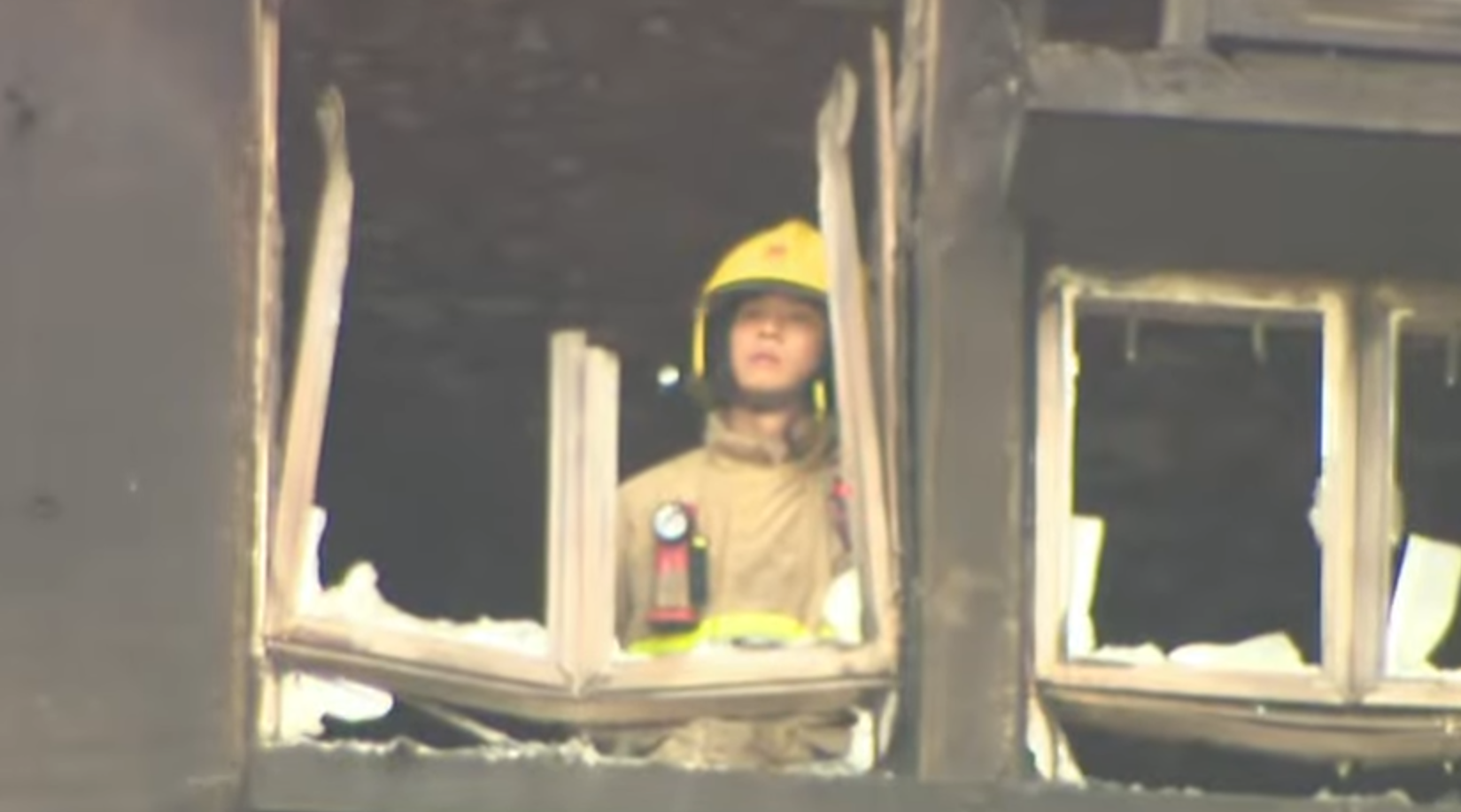 大埔宏福苑五級火,一名消防員登上一個已遭嚴重焚毀、窗框破爛的單位視察,不時望向窗外凝視接近5分鐘,期間若有所思神色凝重咬唇。(有線新聞畫面)