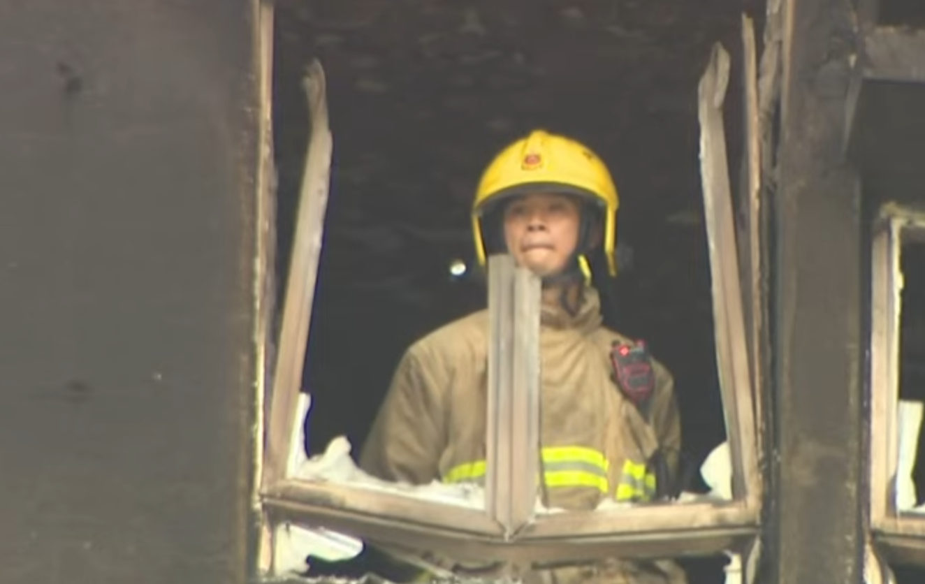 大埔宏福苑五級火,一名消防員登上一個已遭嚴重焚毀、窗框破爛的單位視察,不時望向窗外凝視接近5分鐘,期間若有所思神色凝重咬唇。(有線新聞畫面)