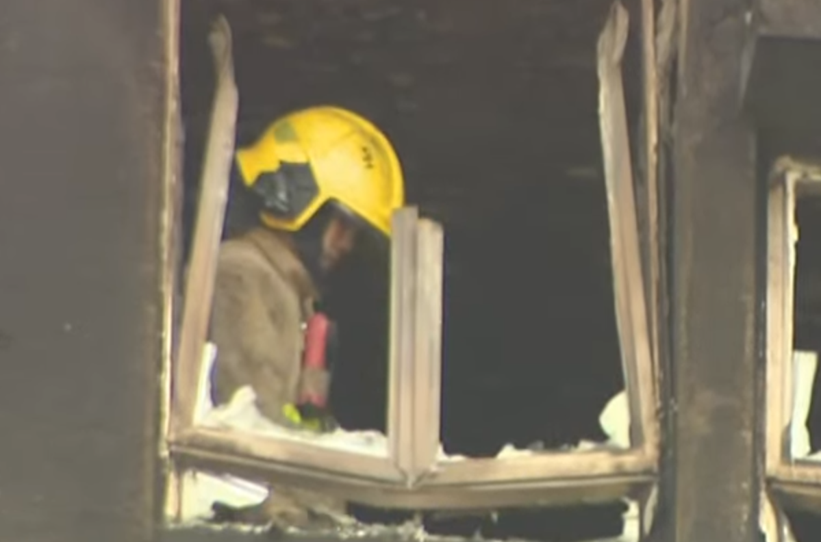 大埔宏福苑五級火,一名消防員登上一個已遭嚴重焚毀、窗框破爛的單位視察,不時望向窗外凝視接近5分鐘,期間若有所思神色凝重咬唇。(有線新聞畫面)