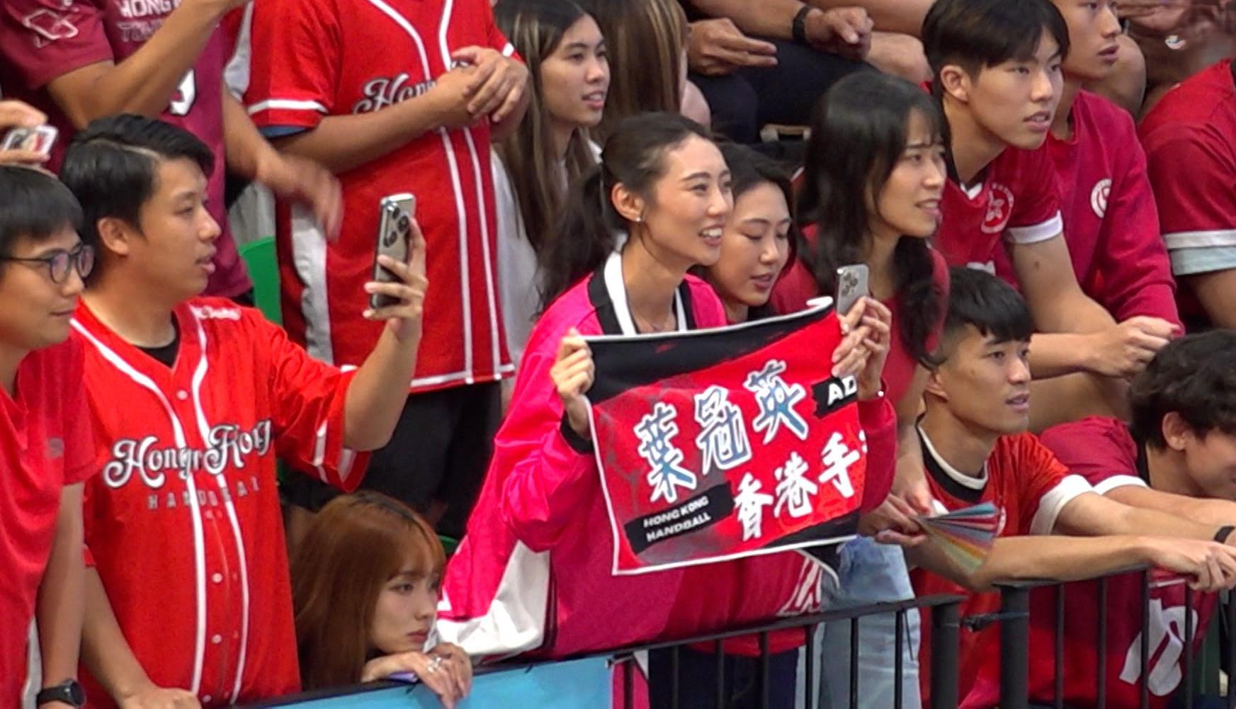 香港手球隊門將葉冠英的太太亦有入場支持,並穿上印有丈夫名字和號碼的球衣打氣。(港台圖片)