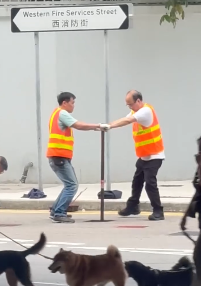 上環西消防街兩名工人在馬路進行維修工作開關水掣,他們面對面、雙手交疊合力轉動閥門的動作極具默契,遠看彷彿是一對正在跳華爾茲舞的拍擋。另外,影片可見附近恰巧有三隻狗路過,成為網民「錯重點」討論對象。(Threads)