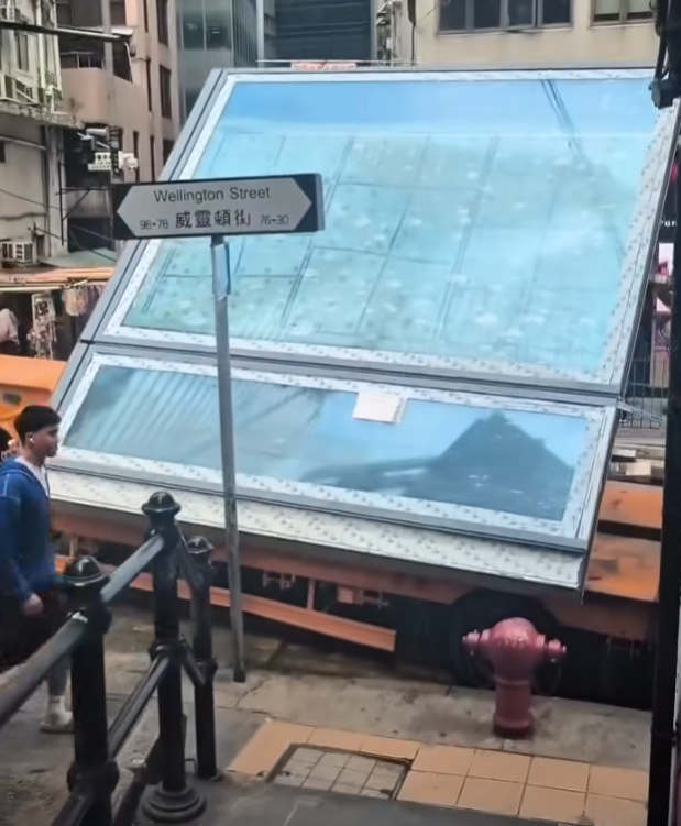 一輛載有玻璃窗等大型建築材料的大型貨車,撞到「威靈頓街」路牌。路牌被撞後傾斜近45度角,最後貨車離開現場,事後引來不少市民及遊客圍觀擺甫士「打卡」拍照。(SH Hong@車cam L(香港群組)FB)