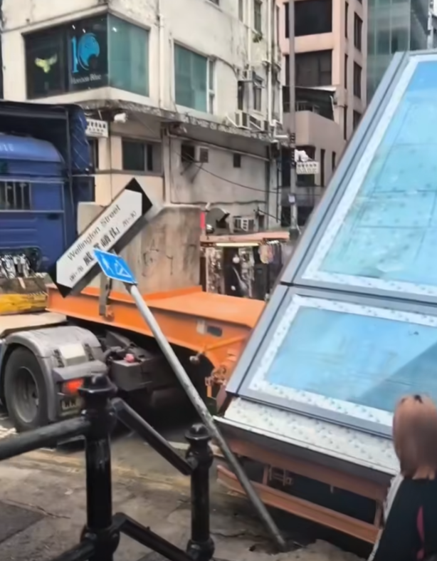 一輛載有玻璃窗等大型建築材料的大型貨車,撞到「威靈頓街」路牌。路牌被撞後傾斜近45度角,最後貨車離開現場,事後引來不少市民及遊客圍觀擺甫士「打卡」拍照。(SH Hong@車cam L(香港群組)FB)