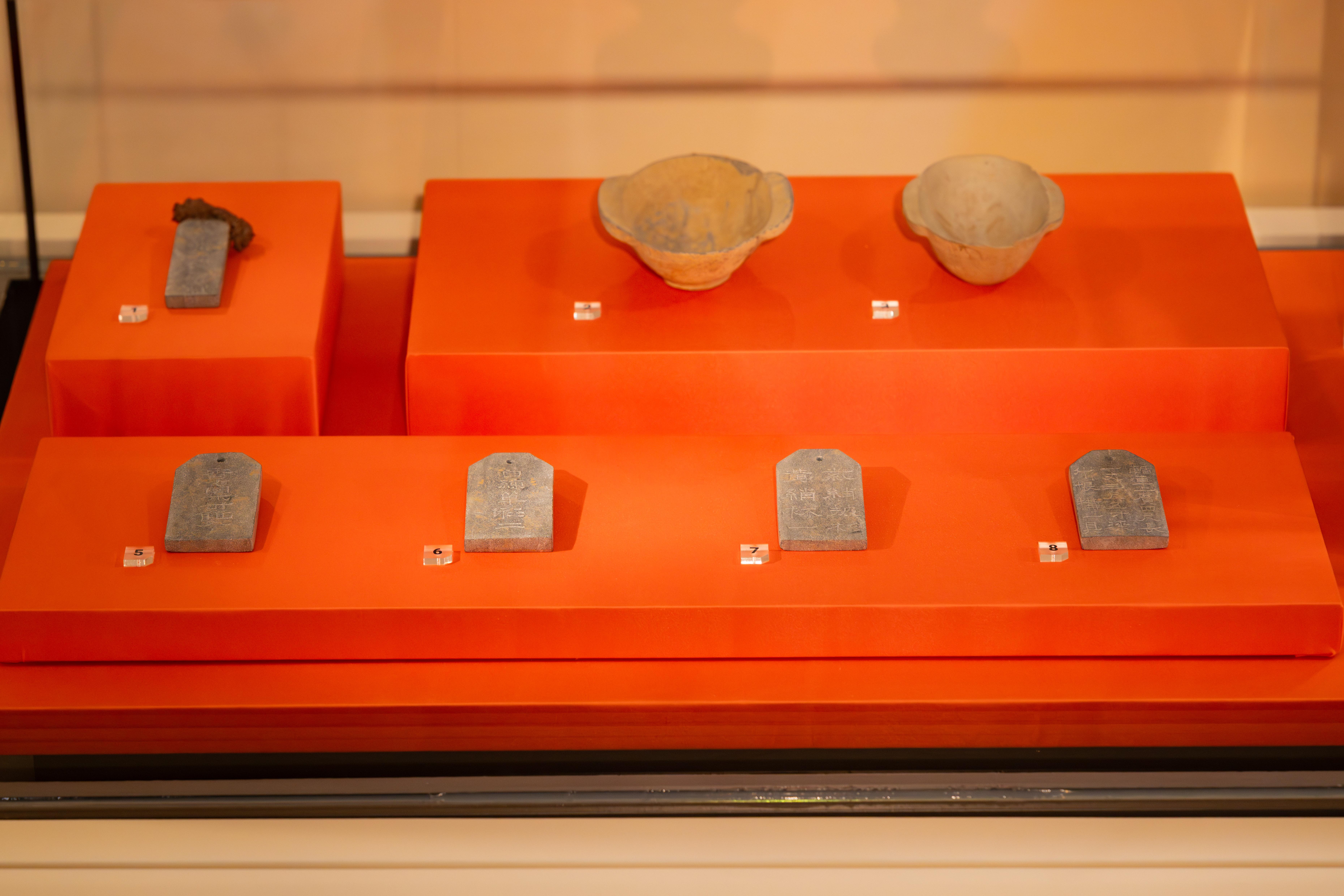 考古曹操展覽,圖示「魏武王常所用挌虎大戟」石牌(複製品)於後排左方、東漢時期陶質耳杯(複製品)於後排中及右方,和刻有隨葬物品名稱及數量的石牌(複製品)於前排。