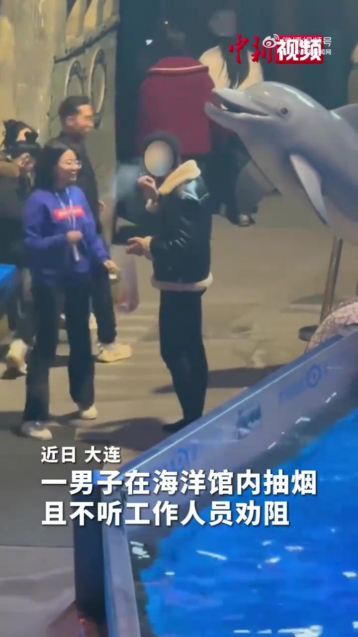 一名男子在水族館內抽煙遭白鯨噴水。(《中國新聞網》)
