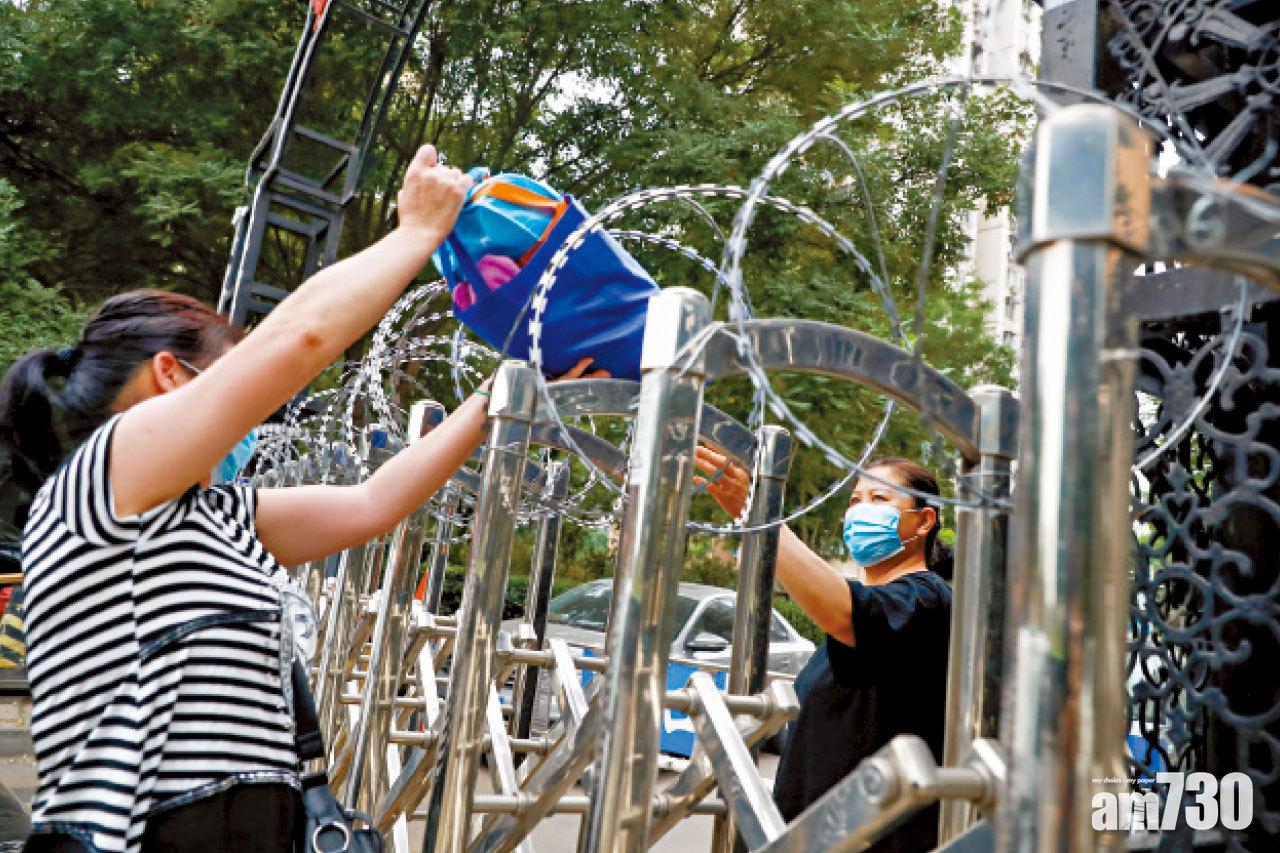 屋苑被封的居民隔著大閘接收親友送來的生活用品。(路透社)