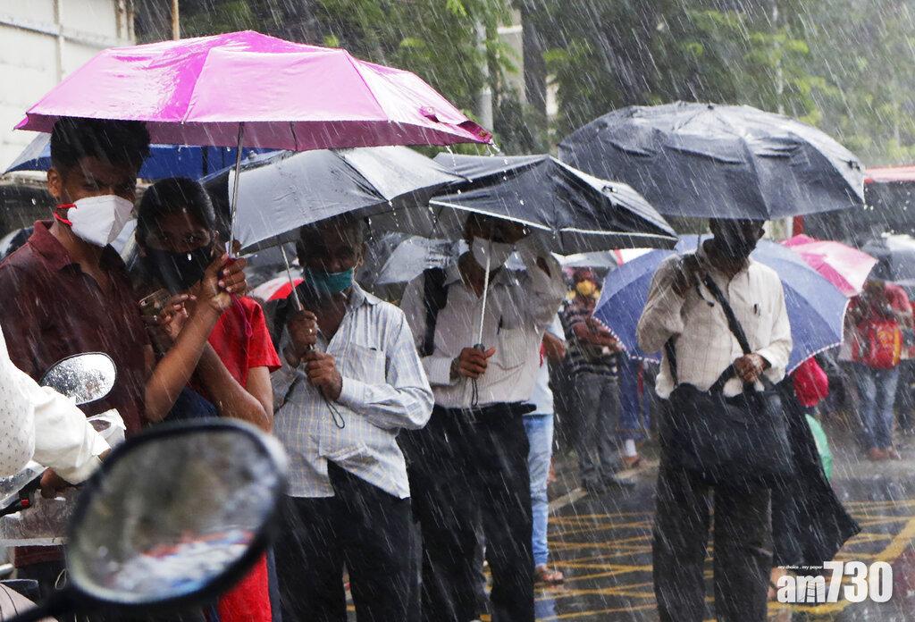 印度疫情失控。圖為孟買民眾冒雨等巴士。(美聯社)