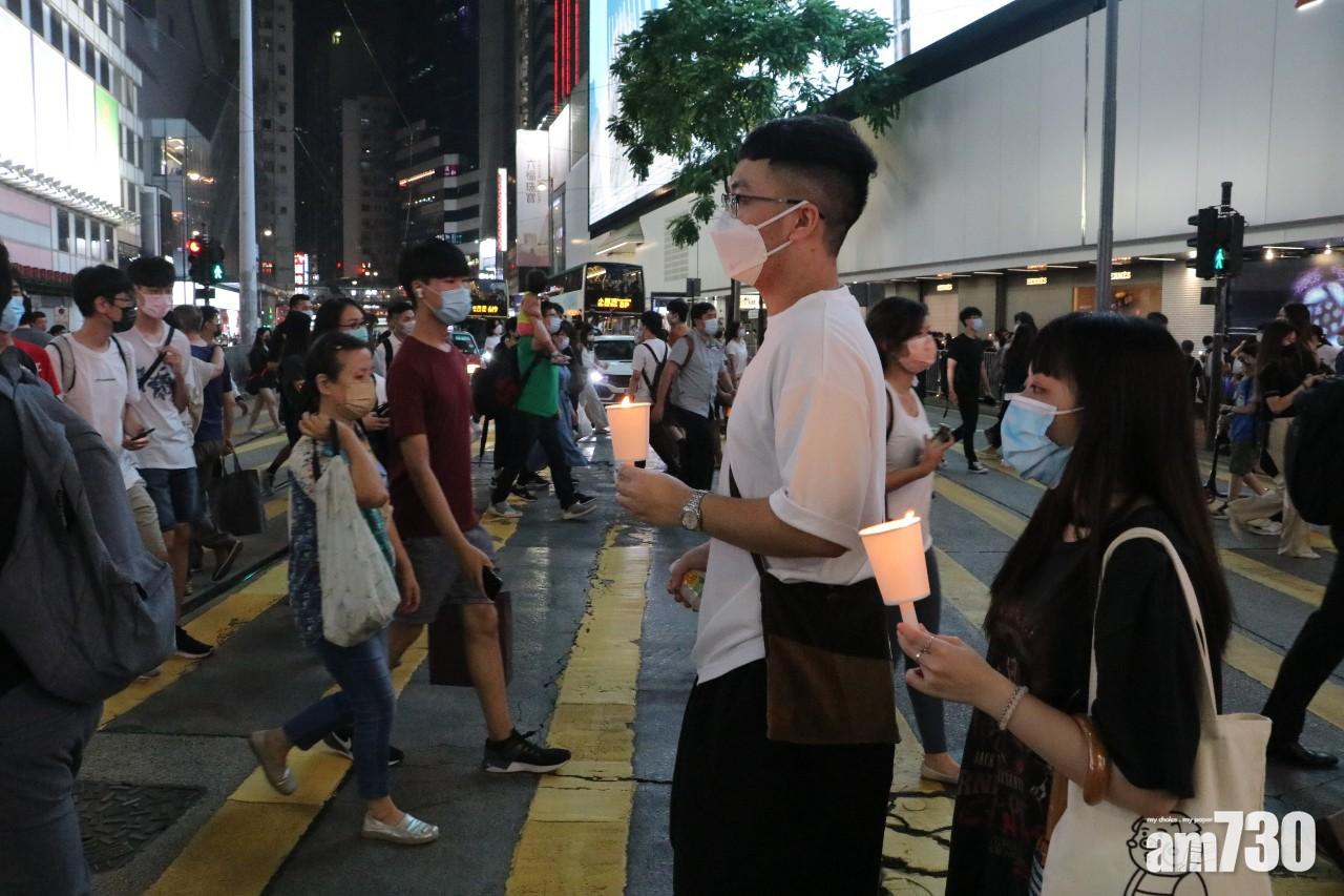 有男女手持燭光在銅鑼灣崇光百貨外過馬路。(林俊源攝)