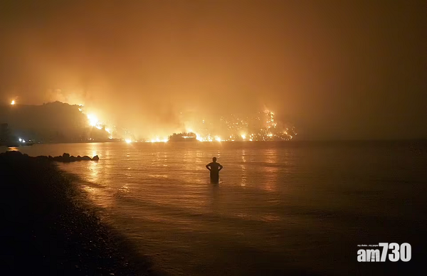在埃維亞島,村民站在水中遙望陷入火海的山林。(美聯社)