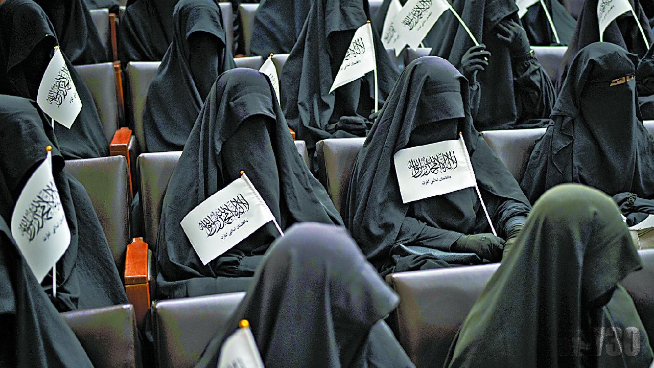 一群婦女穿著袍罩、手持塔利班旗幟,上周六在喀布爾大學表示支持新教育規定。