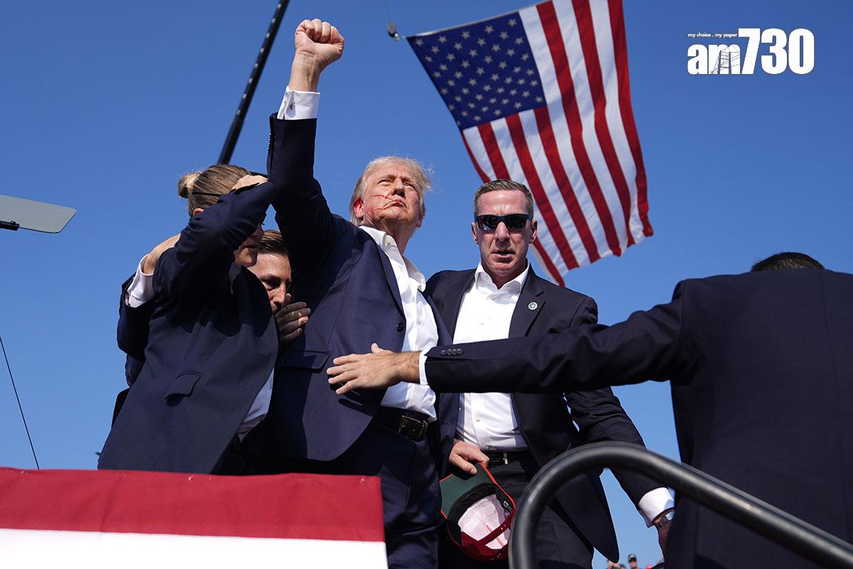 特朗普遇刺後由大批特工護送離開,其間他不忘高舉雙手示意不認輸。(美聯社)