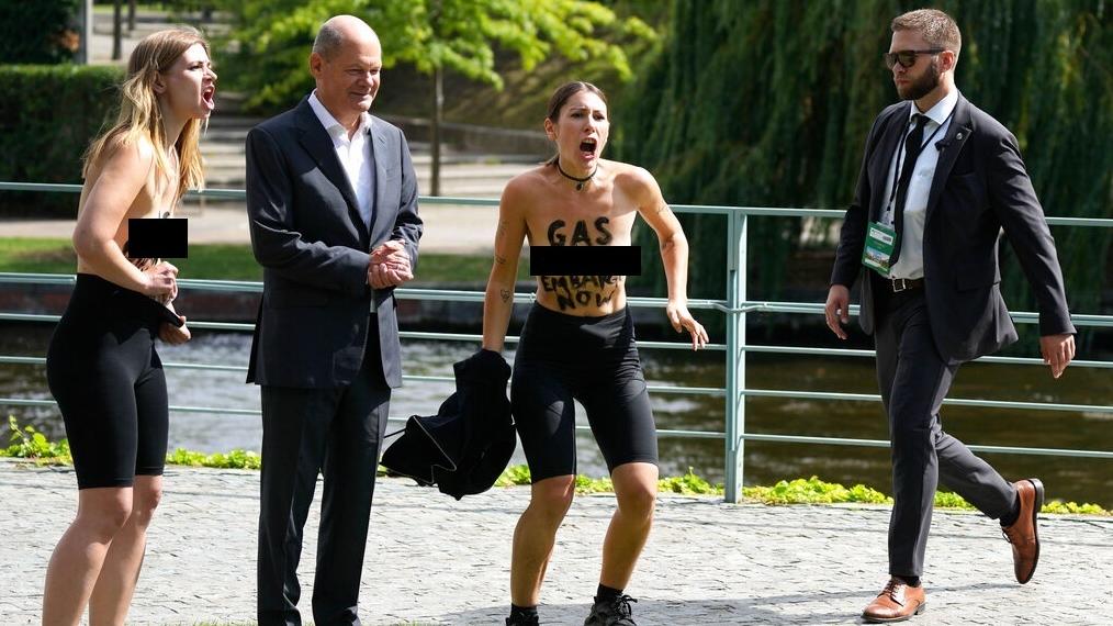 兩名女子假裝與肖爾茨合照，卻突然脫掉上衣並高喊抗議口號。(美聯社)