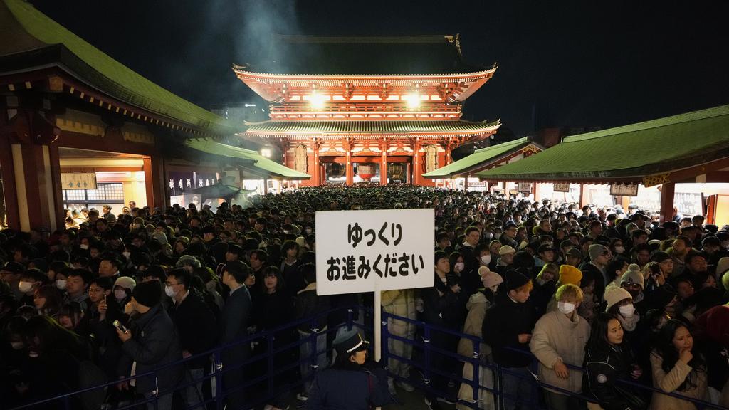 大批民眾元旦凌晨到東京淺草寺祈福，工作人員舉牌呼籲民眾「緩慢移動」。(美聯社)