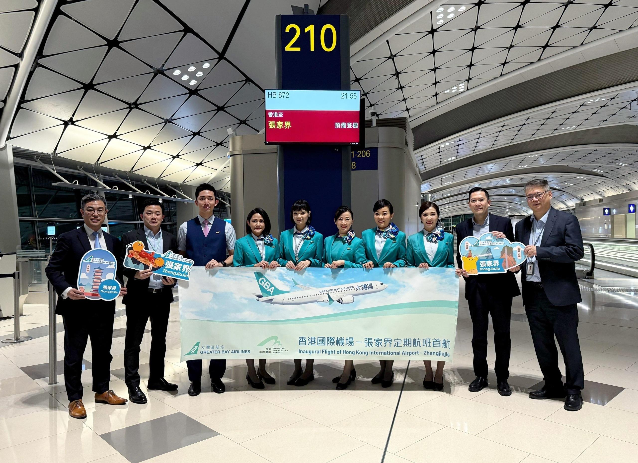 大灣區航空張家界定期航班亦於同日晚上投入服務。香港機場管理局助理經理—航空樞紐發展王文遠先生（左二）在大灣區航空管理層代表陪同下，親臨香港國際機場登機閘口為首航班機的乘客及機組人員送行，以表對新航線的支持。