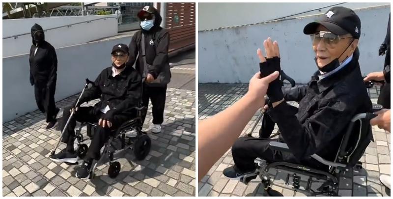 片中的謝賢戴上黑色Cap帽、黑超，又以全黑造型坐在輪椅上於尖沙咀散步，身邊有兩位同樣以全黑打扮的人在身旁陪伴及照顧他(影片截圖)