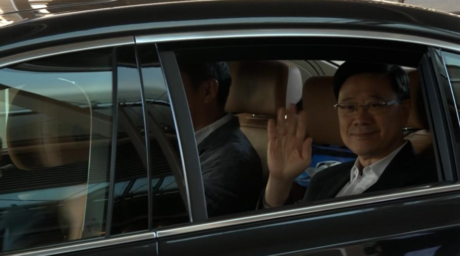 李家超返抵本港，乘坐專車離開時向傳媒揮手。(港台圖片）